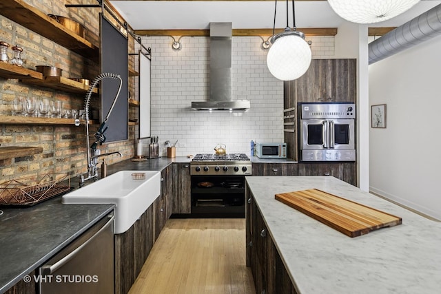 kitchen featuring a sink, tasteful backsplash, stainless steel appliances, wall chimney exhaust hood, and dark brown cabinets