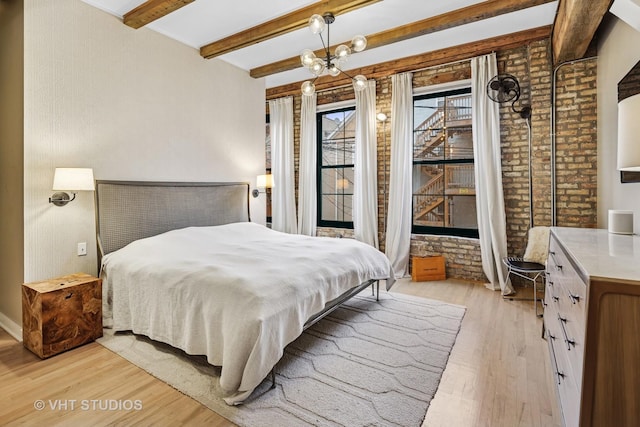 bedroom with light wood-type flooring, a notable chandelier, beamed ceiling, and brick wall