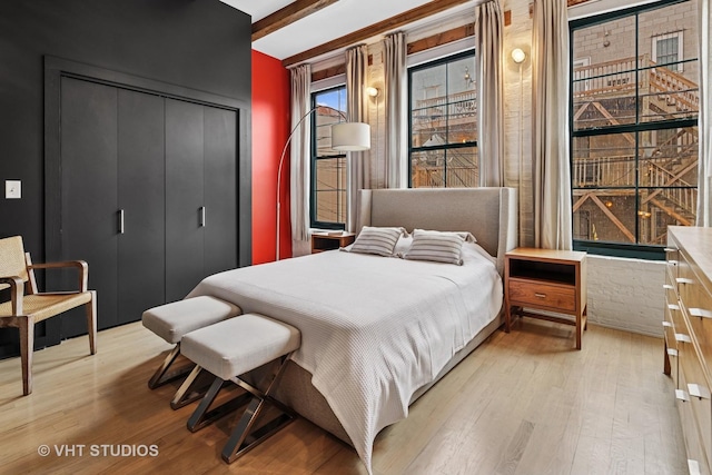 bedroom with a closet, beam ceiling, and light wood-type flooring