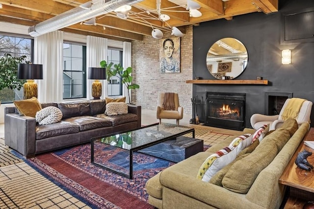 living area featuring beamed ceiling, brick wall, and a warm lit fireplace