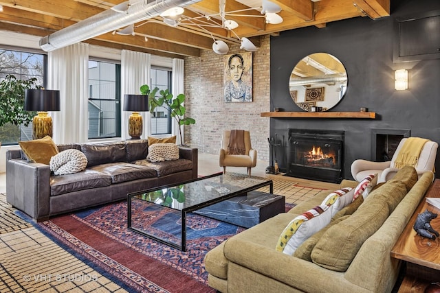 living area featuring beamed ceiling, a glass covered fireplace, and brick wall