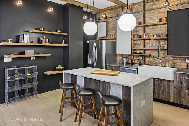 kitchen with a sink, a center island, stainless steel appliances, a breakfast bar area, and light wood finished floors