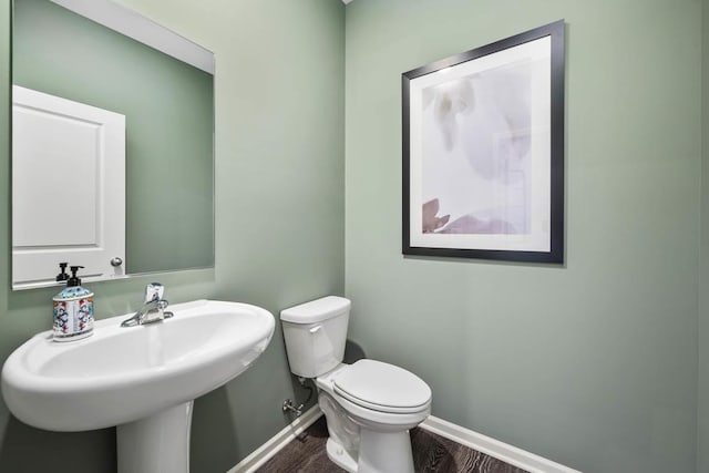 half bathroom with toilet, wood finished floors, baseboards, and a sink