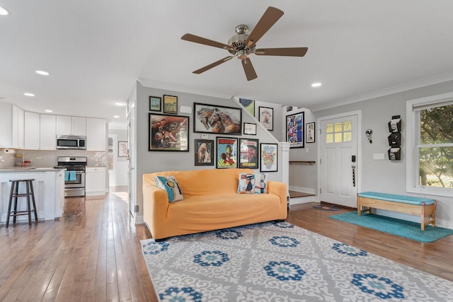 living area featuring recessed lighting, light wood-type flooring, ornamental molding, and a ceiling fan