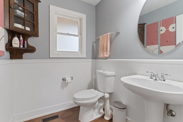 half bathroom featuring wood finished floors, a wainscoted wall, visible vents, a sink, and toilet