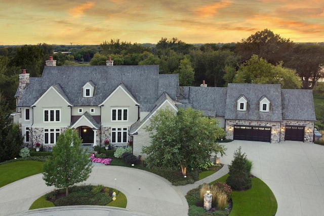 cape cod house featuring a garage, stone siding, and curved driveway