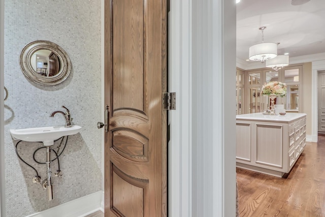 bathroom featuring ornamental molding, a sink, wood finished floors, wallpapered walls, and baseboards