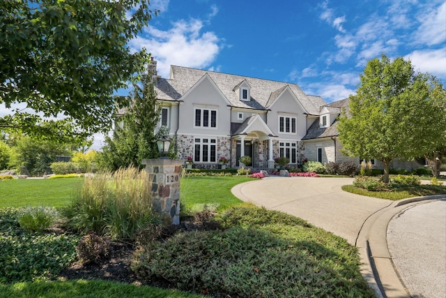 view of front facade featuring a front yard, driveway, a chimney, stucco siding, and stone siding