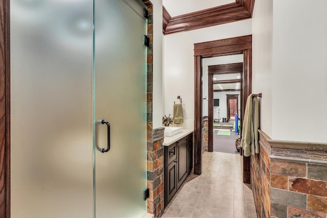 full bath with crown molding, vanity, wainscoting, a stall shower, and tile walls