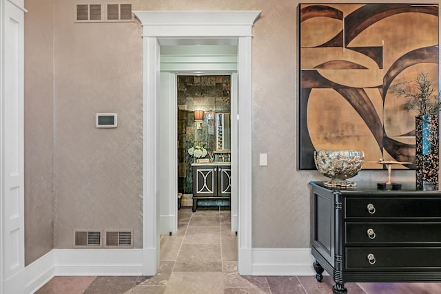 hallway with visible vents, baseboards, stone tile flooring, and a textured wall