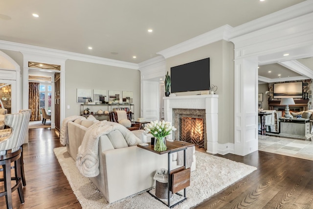 living area featuring recessed lighting, ornamental molding, a warm lit fireplace, and wood finished floors