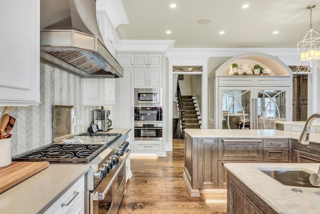 kitchen featuring wall chimney range hood, wood finished floors, stainless steel appliances, crown molding, and light countertops