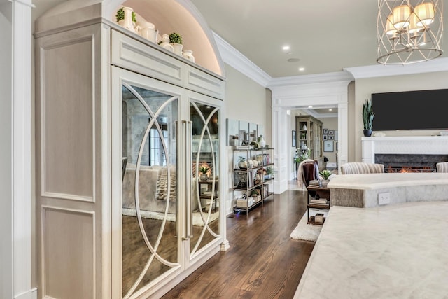 interior space featuring dark wood-type flooring, ornamental molding, access to outside, a warm lit fireplace, and an inviting chandelier