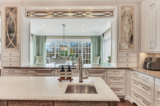 kitchen featuring a sink, crown molding, light stone countertops, decorative backsplash, and dark wood-style flooring