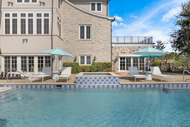 rear view of house with a fenced in pool, stucco siding, a balcony, stone siding, and a jacuzzi