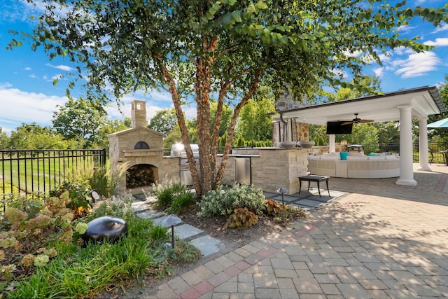 view of patio with ceiling fan, area for grilling, fence, and an outdoor stone fireplace