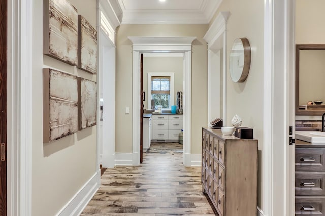 hallway featuring crown molding, light wood-style floors, baseboards, and a sink