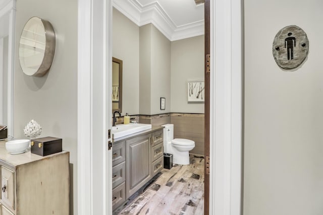 bathroom with toilet, vanity, ornamental molding, wainscoting, and tile walls