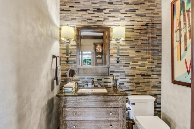 half bath with backsplash, toilet, and vanity