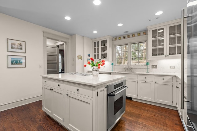 kitchen with a sink, light stone countertops, stainless steel oven, decorative backsplash, and dark wood-style flooring