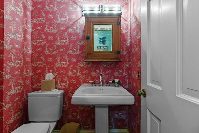 half bath with wallpapered walls and toilet