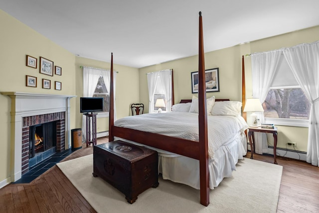 bedroom with a baseboard radiator, baseboards, a brick fireplace, and wood finished floors