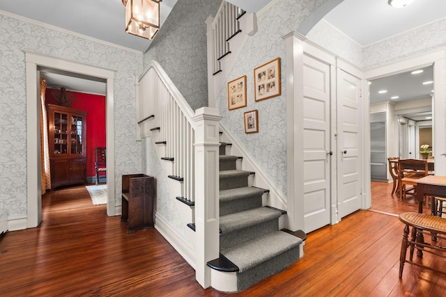 stairway with wood-type flooring, arched walkways, crown molding, wallpapered walls, and baseboards