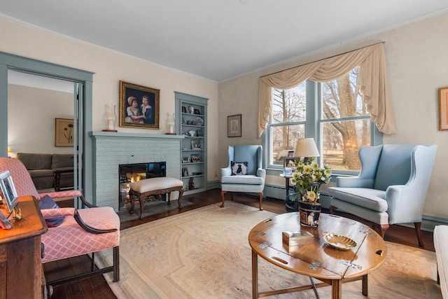 living area featuring built in features, a baseboard radiator, a fireplace, and wood finished floors