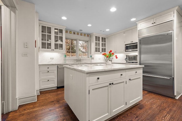 kitchen featuring a kitchen island, dark wood-style floors, stainless steel appliances, white cabinets, and light stone countertops