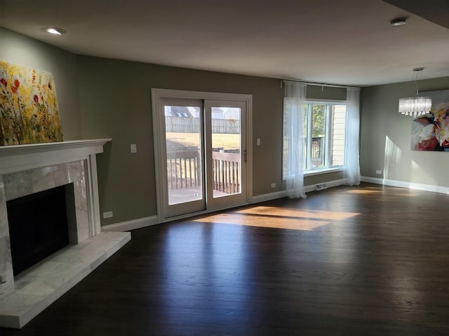 unfurnished living room featuring a notable chandelier, wood finished floors, baseboards, and a premium fireplace