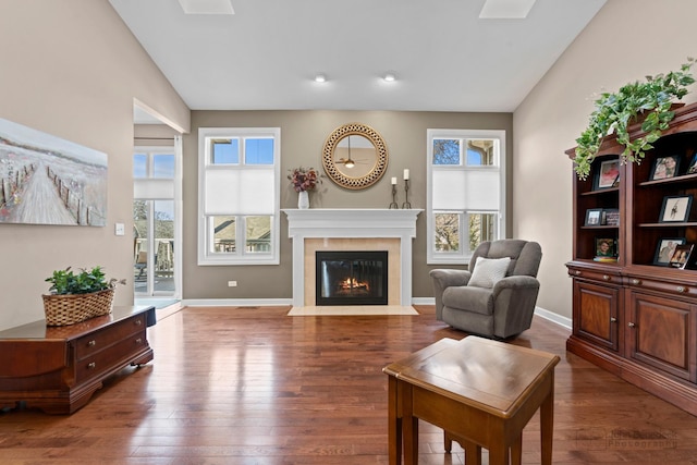 living area with hardwood / wood-style flooring, a fireplace with flush hearth, baseboards, and vaulted ceiling