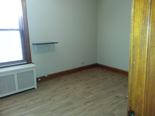 unfurnished room with radiator heating unit, baseboards, and wood finished floors