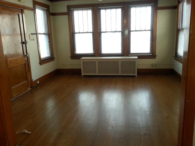 spare room featuring radiator heating unit, baseboards, and wood finished floors