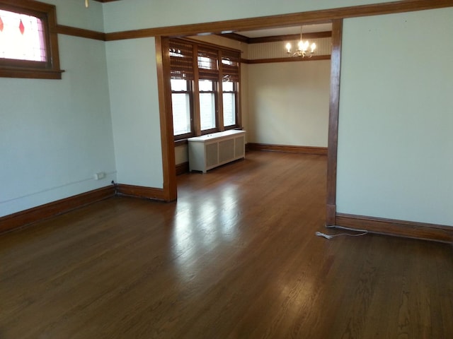 spare room featuring an inviting chandelier, radiator heating unit, wood finished floors, and baseboards