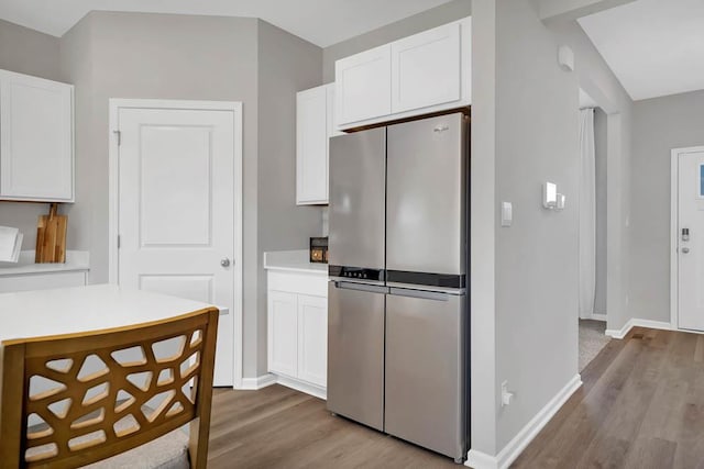 kitchen with baseboards, light wood finished floors, freestanding refrigerator, light countertops, and white cabinetry