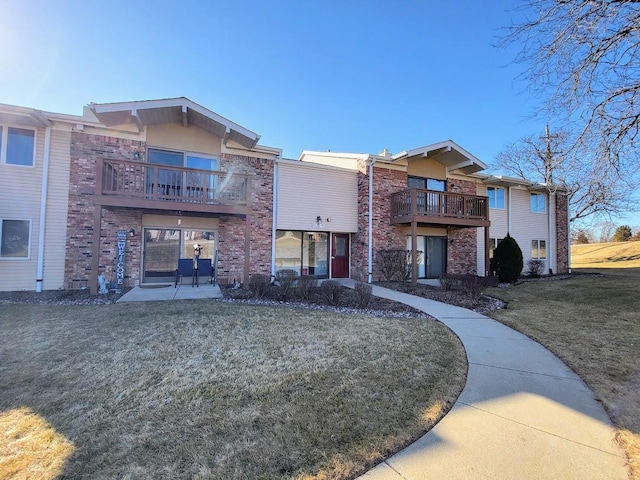 exterior space featuring brick siding, a balcony, a front lawn, and a patio area