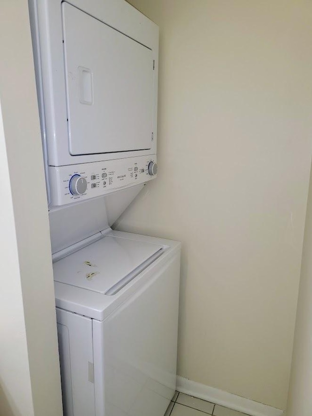 clothes washing area with laundry area, light tile patterned floors, baseboards, and stacked washing maching and dryer