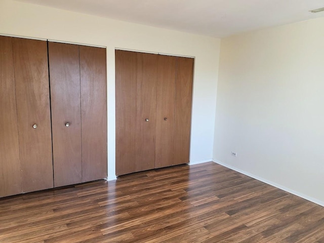 unfurnished bedroom with visible vents, two closets, baseboards, and wood finished floors