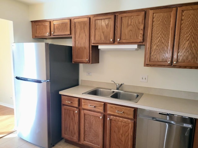 kitchen featuring brown cabinetry, stainless steel appliances, light countertops, and a sink