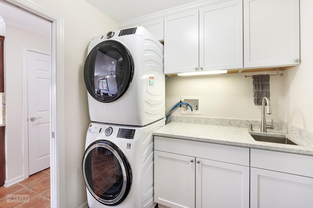 clothes washing area with a sink, light tile patterned floors, cabinet space, and stacked washing maching and dryer