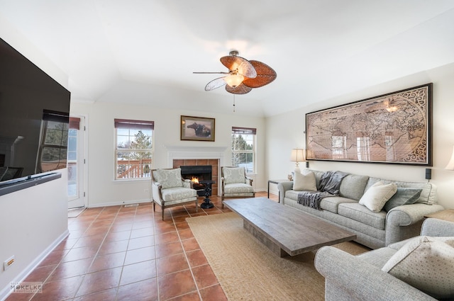 living area with baseboards, dark tile patterned floors, lofted ceiling, a tile fireplace, and a ceiling fan