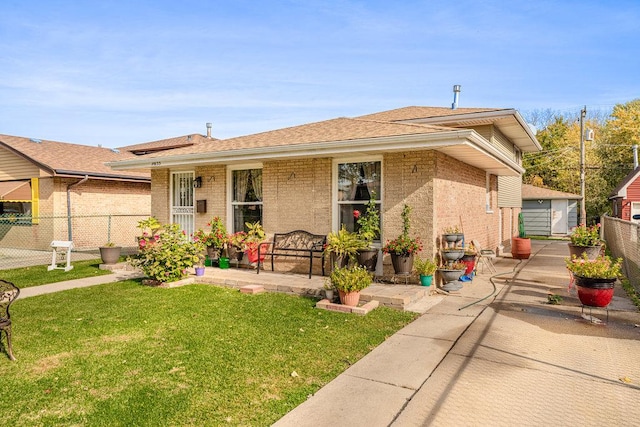 view of front of property with a patio, fence, roof with shingles, a front yard, and brick siding