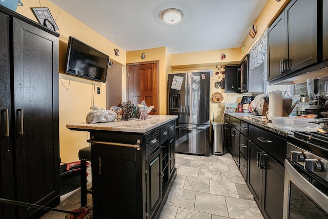 kitchen with a kitchen island, appliances with stainless steel finishes, light stone countertops, and dark cabinets