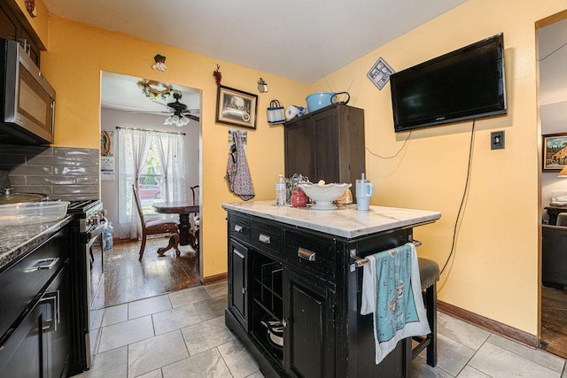 kitchen with backsplash, a kitchen island, dark cabinetry, appliances with stainless steel finishes, and ceiling fan