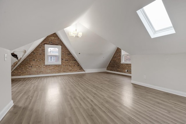 bonus room featuring wood finished floors, baseboards, brick wall, an inviting chandelier, and lofted ceiling with skylight