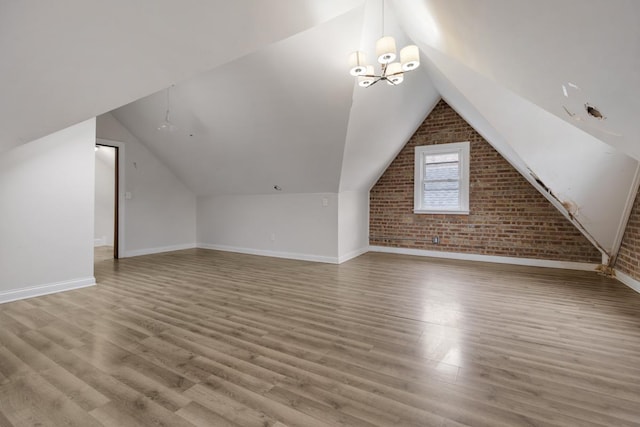 additional living space with wood finished floors, baseboards, brick wall, vaulted ceiling, and a notable chandelier