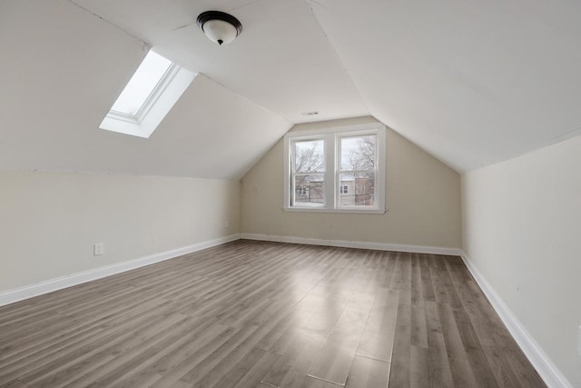 bonus room with vaulted ceiling with skylight, wood finished floors, and baseboards