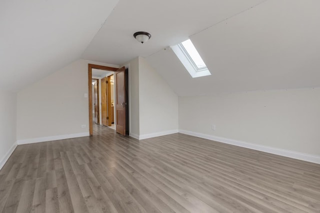 additional living space with baseboards, vaulted ceiling with skylight, and light wood finished floors