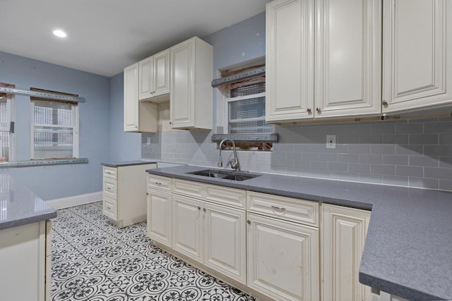 kitchen with a sink, baseboards, backsplash, and white cabinets