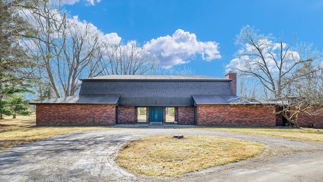 view of front facade featuring brick siding, a chimney, driveway, and roof with shingles